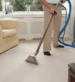 Professional carpet cleaner using a hot-water extraction wand and hose machine in a living room in Worcester, MA.