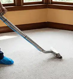 Steam carpet cleaning technician using a hot-water extraction wand on a residential carpet, wearing blue protective shoe covers Worcester, MA.