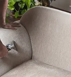 Professional upholstery cleaner deep-cleaning a fabric sofa with a handheld extraction tool and hose Worcester, MA.